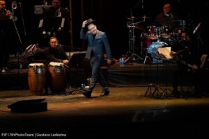 Rubén Blades vestido de negro con sombrero en el escenario con su orquesta