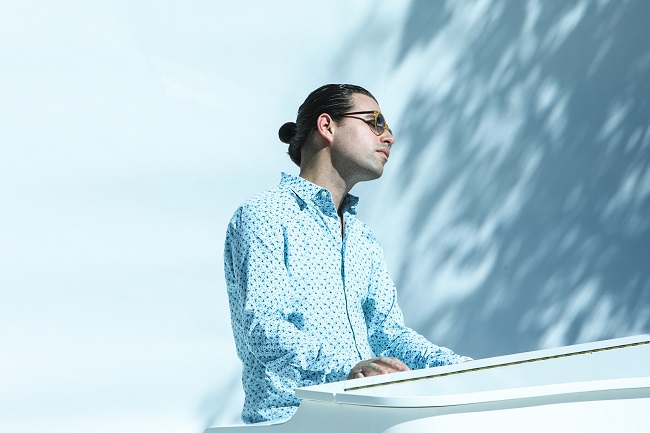 Alfredo Rodríguez con camisa azul sentado frente a un piano blanco