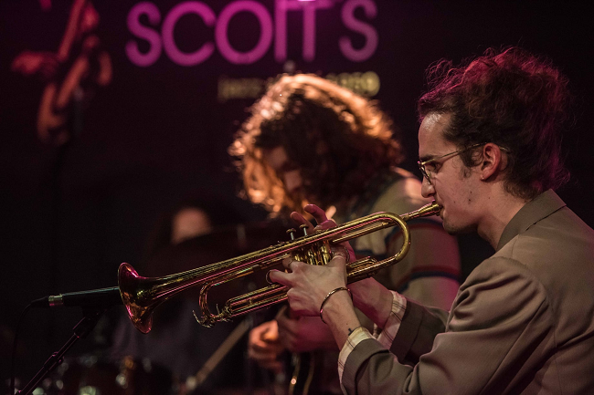 Trompetista vestido de traje beige en El club de Jazz Ronnie Scott's 